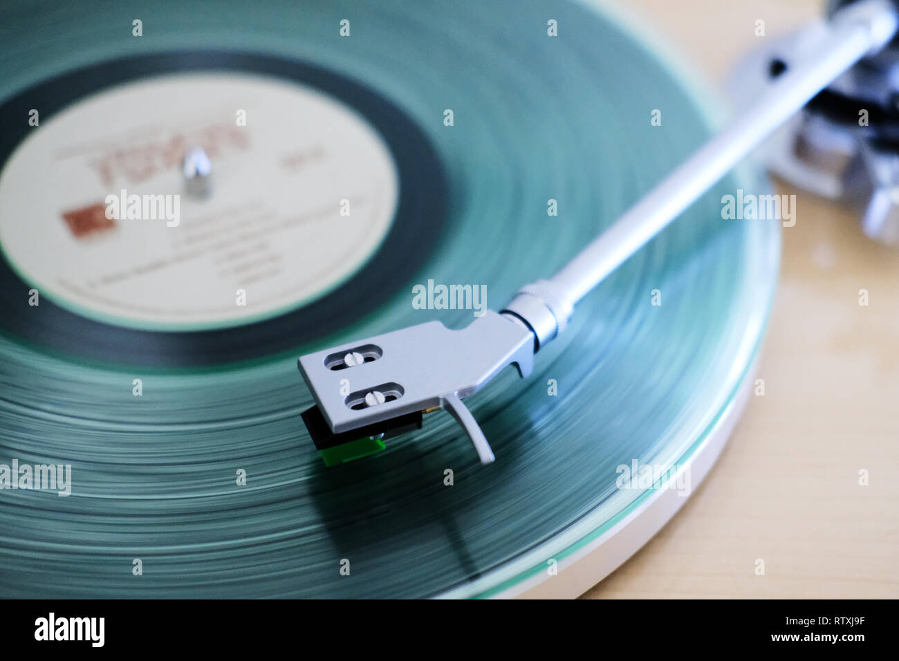 A clear vinyl long playing record on a turntable with a needle arm on the record track playing Stock Photo