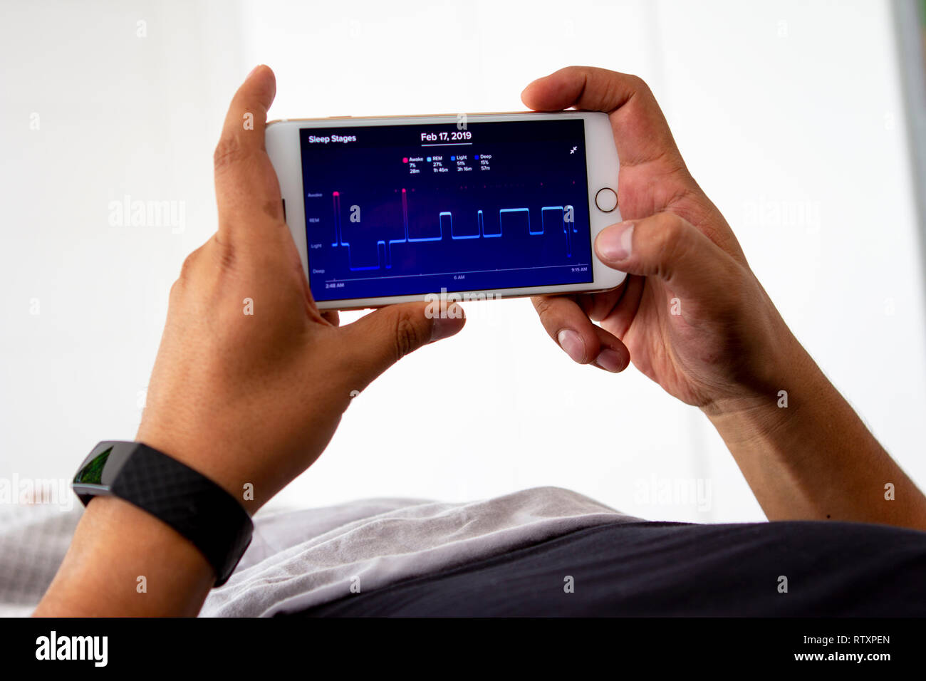 Lima, Peru - February 20 2019: Man waking up in the bed and monitoring his sleep night with a sleep-tracking app and a fitbit activity tracker wearabl Stock Photo