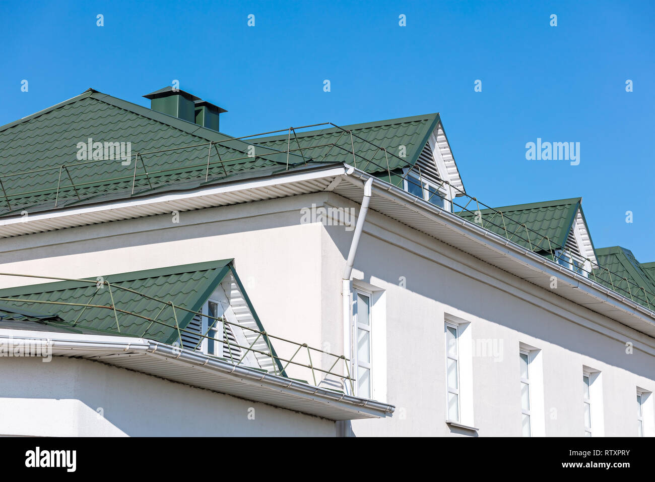 house facade. green rooftop with white metal gutter and downspout. blue sky background Stock Photo