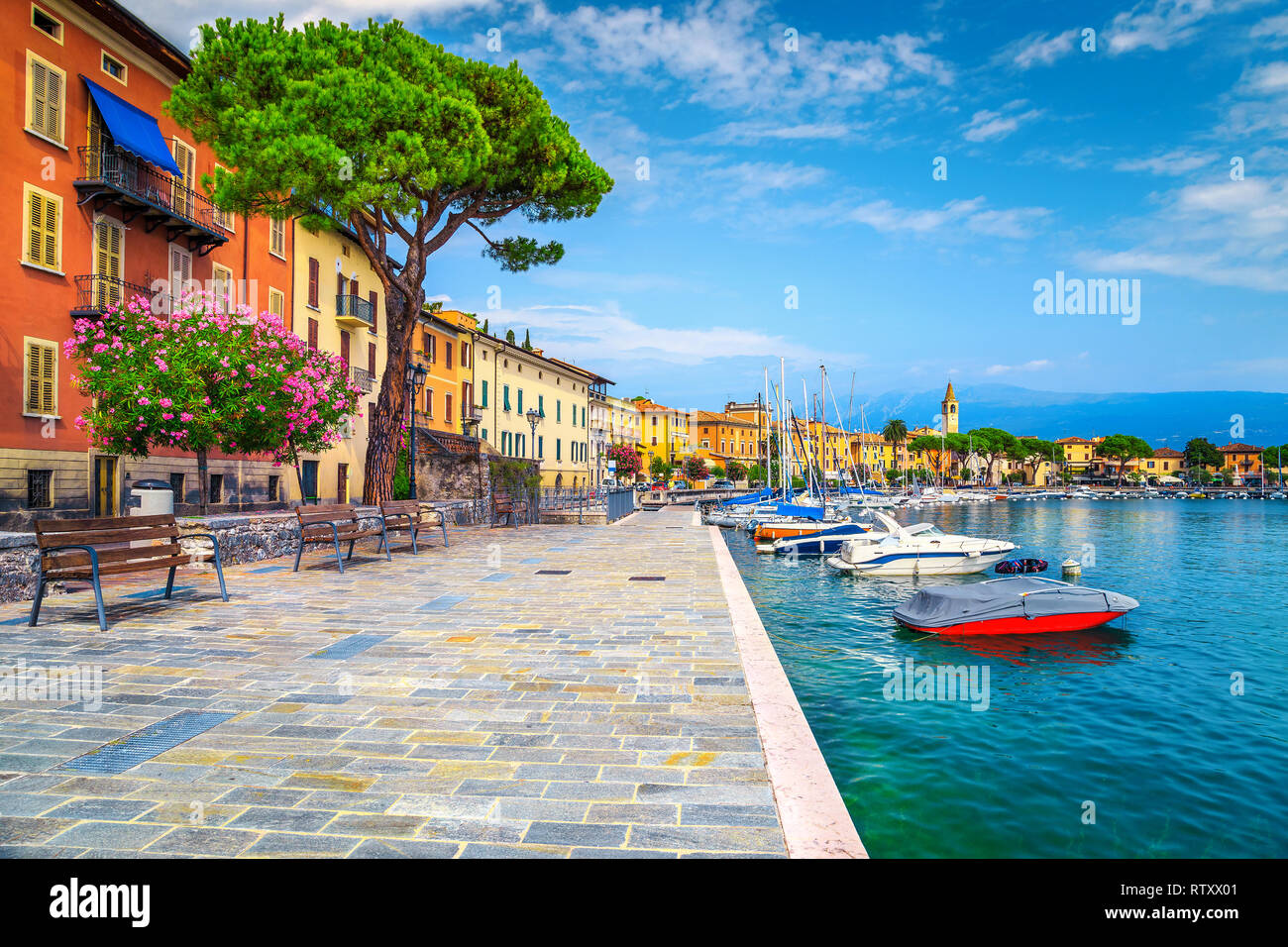 Wonderful paved walkway with colorful mediterranean flowers. Luxury yachts, boats and sailing boats in the majestic harbor of Toscolano-Maderno, lake  Stock Photo
