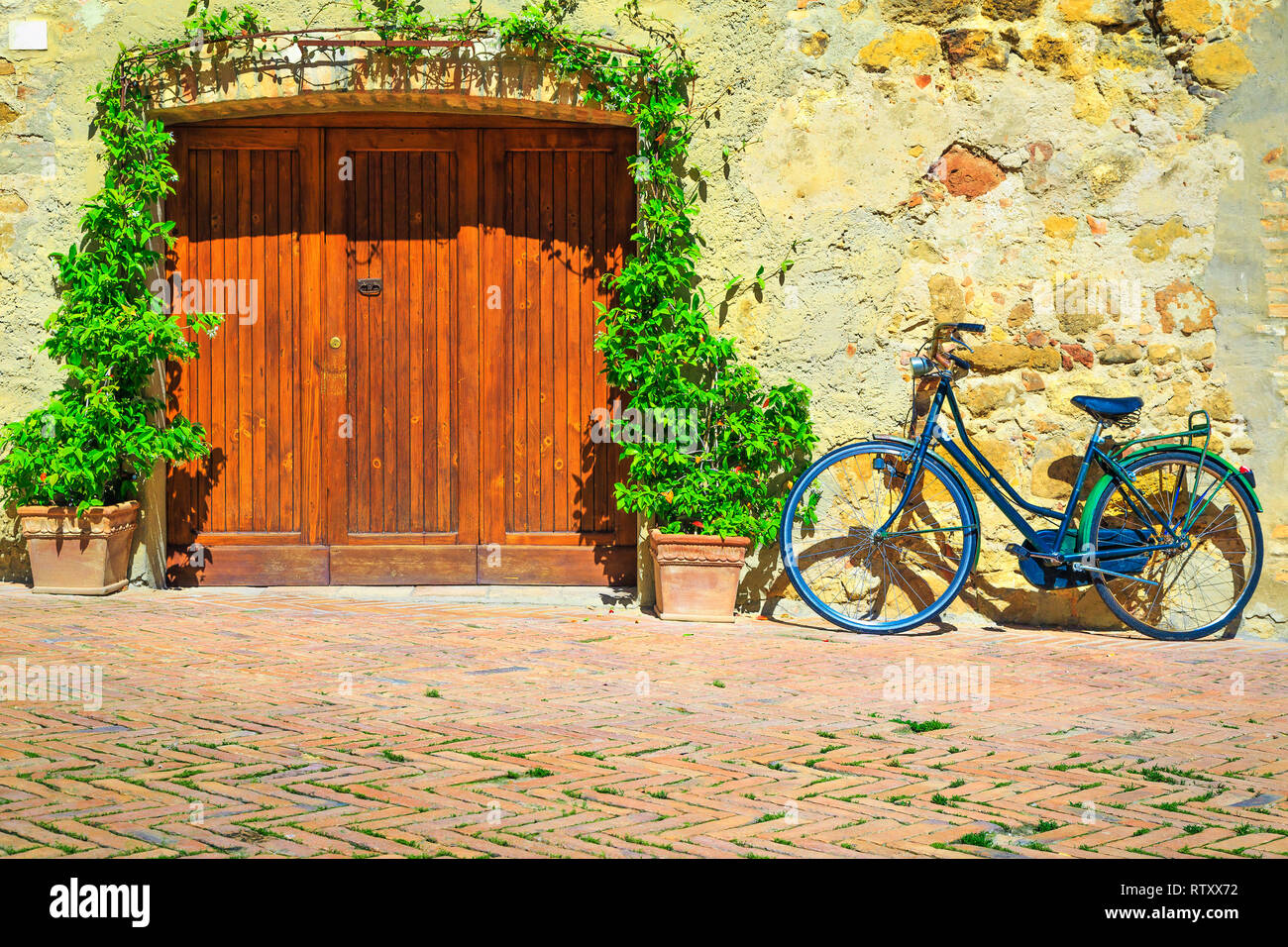 Spectacular Tuscany street view. Entrance and wooden door decorated with jasmine flowers. Old retro bicycle parked in the street, Pienza, Tuscany, Ita Stock Photo