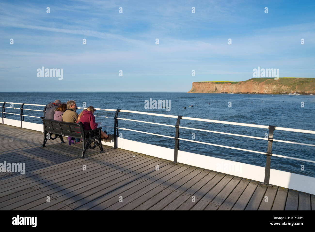 Family sat on bench on the pier at Saltburn-by-the-sea, North Yorkshire, England. Enjoying the view on a sunny spring afternoon. Stock Photo