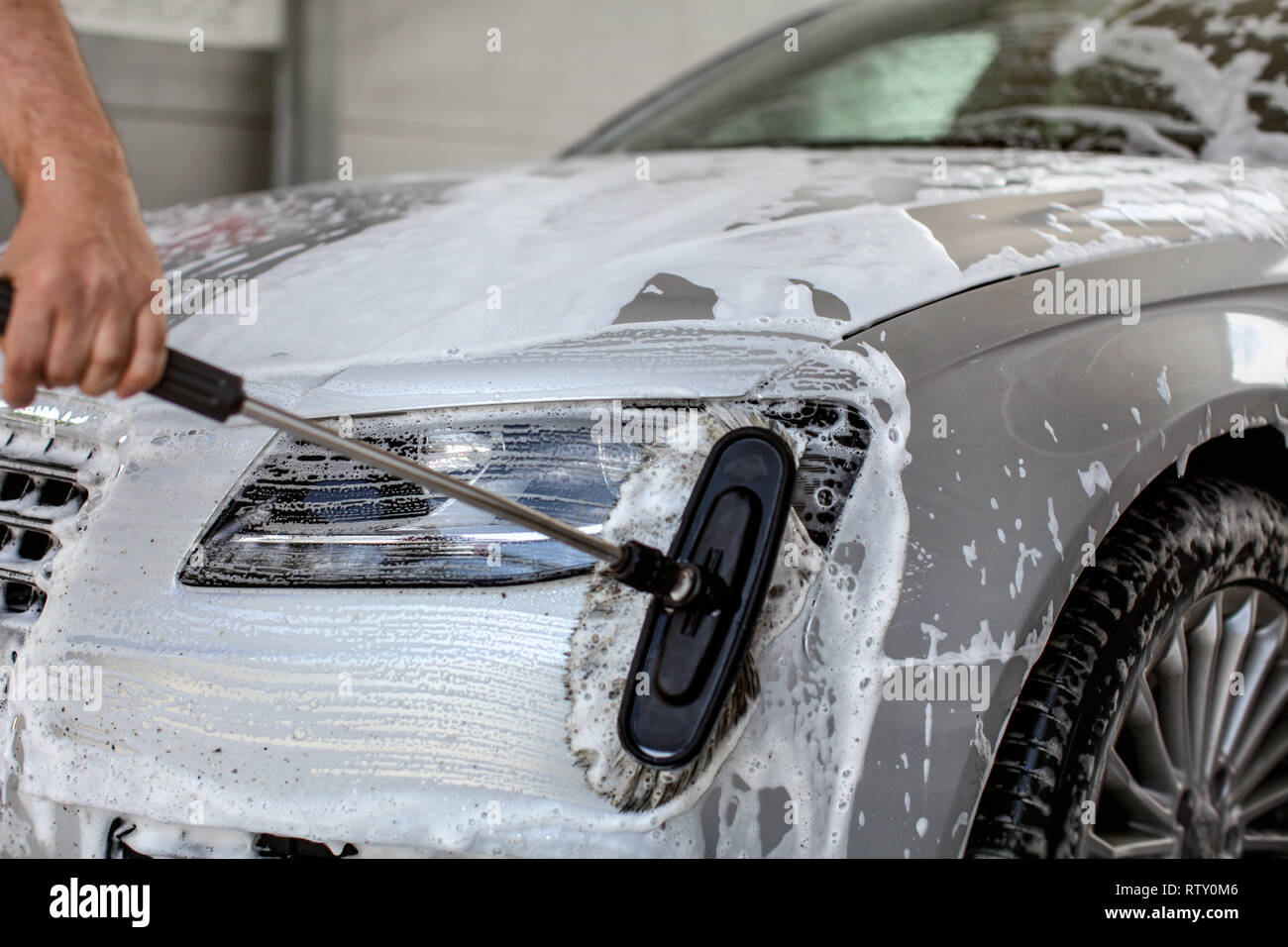 Front light of silver car washed in self serve carwash, man hand holding brush, cleaning the