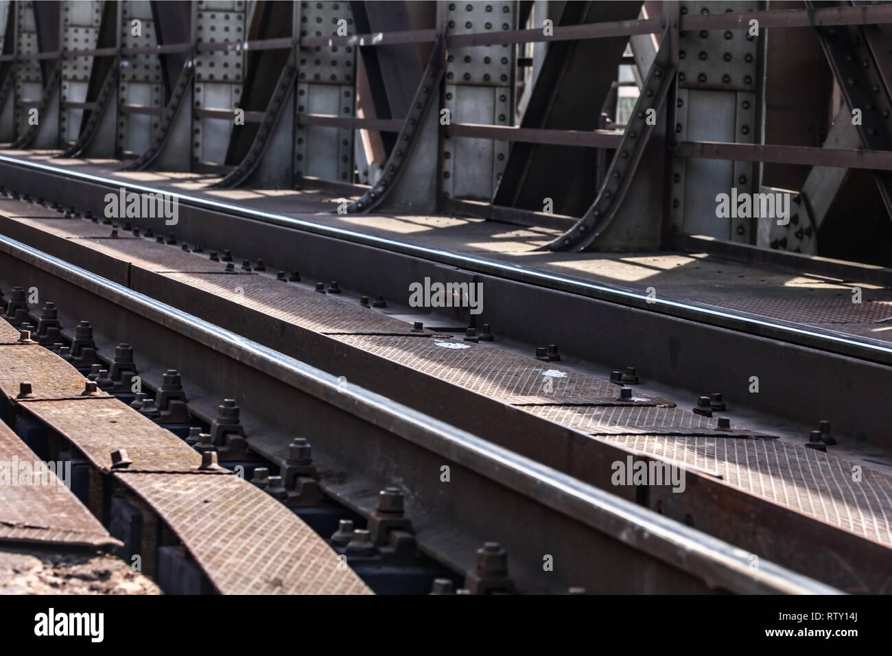 Detail on railway tracks at steel rail bridge lit by sun. Stock Photo