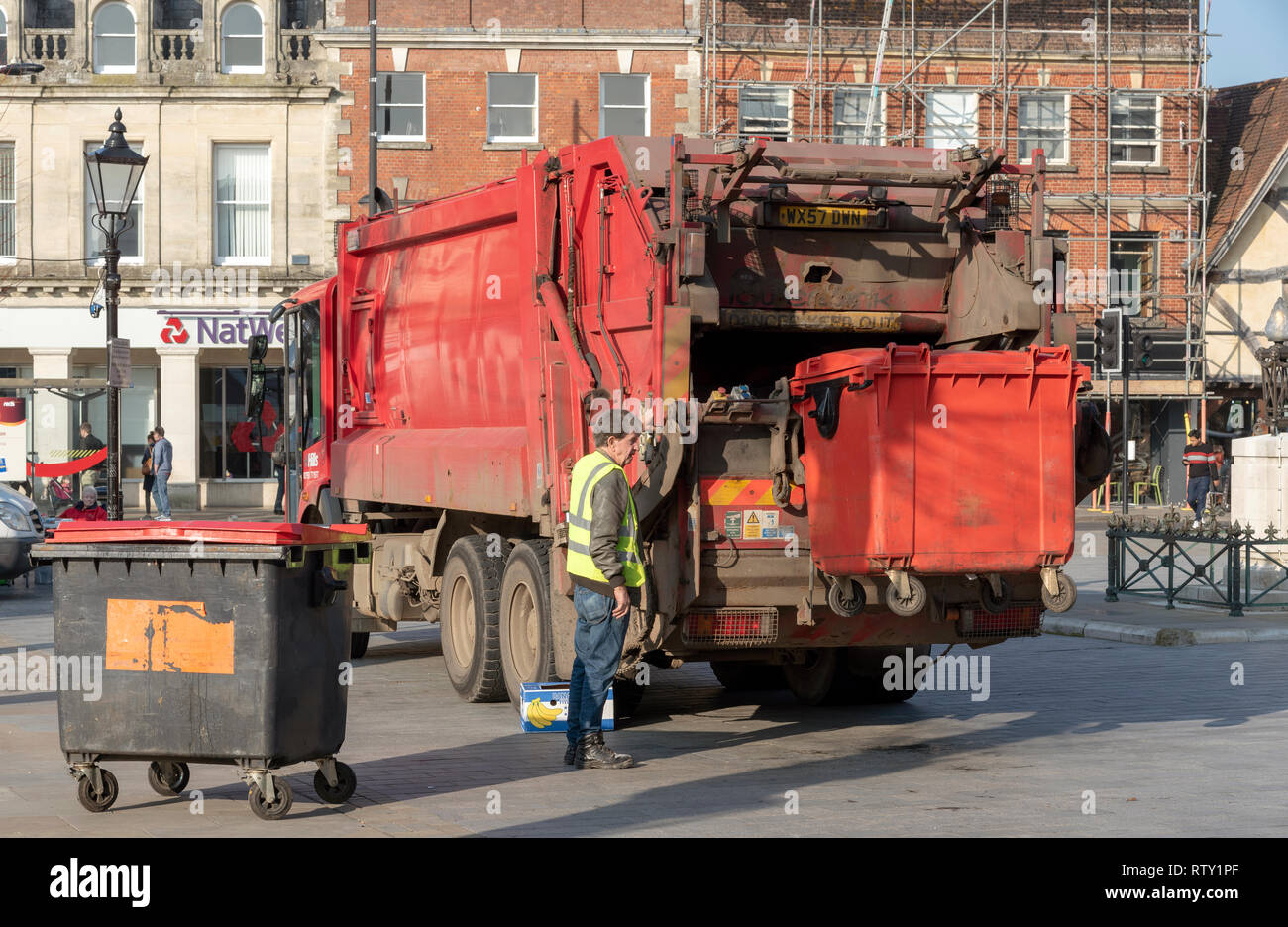 Salisbury, Wiltshire, England, UK. February 2019. Operative loading a commercial size red refuse bin into a truck in the city centre. Stock Photo