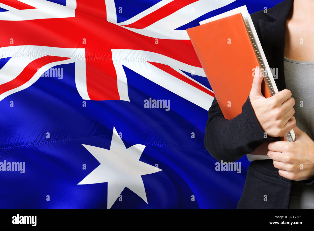 Learning language concept. Young woman standing with the Heard Island and Mcdonald Islands flag in the background. Teacher holding books, orange blank Stock Photo