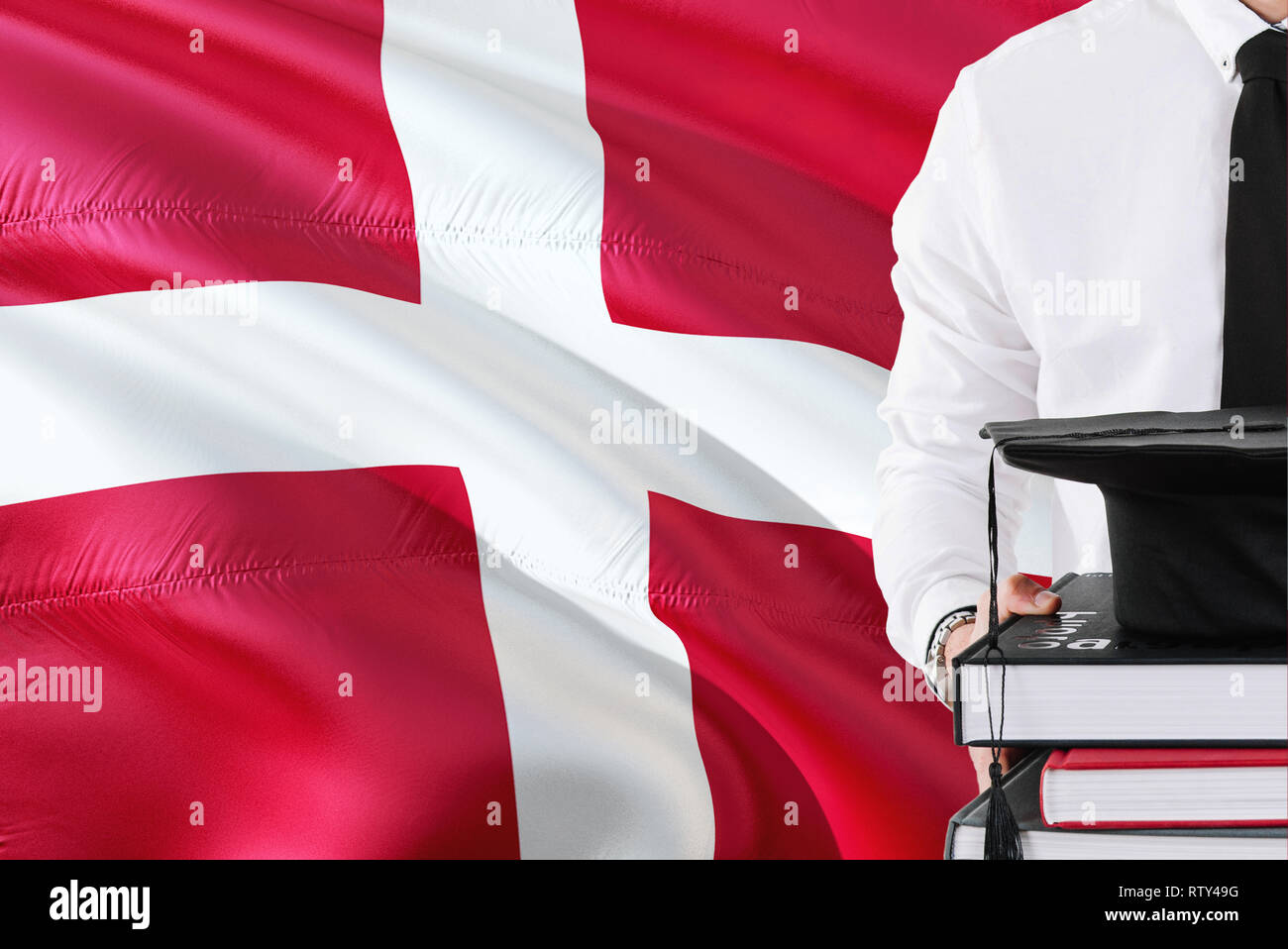 Successful Danish student education concept. Holding books and graduation cap over Denmark flag background. Stock Photo