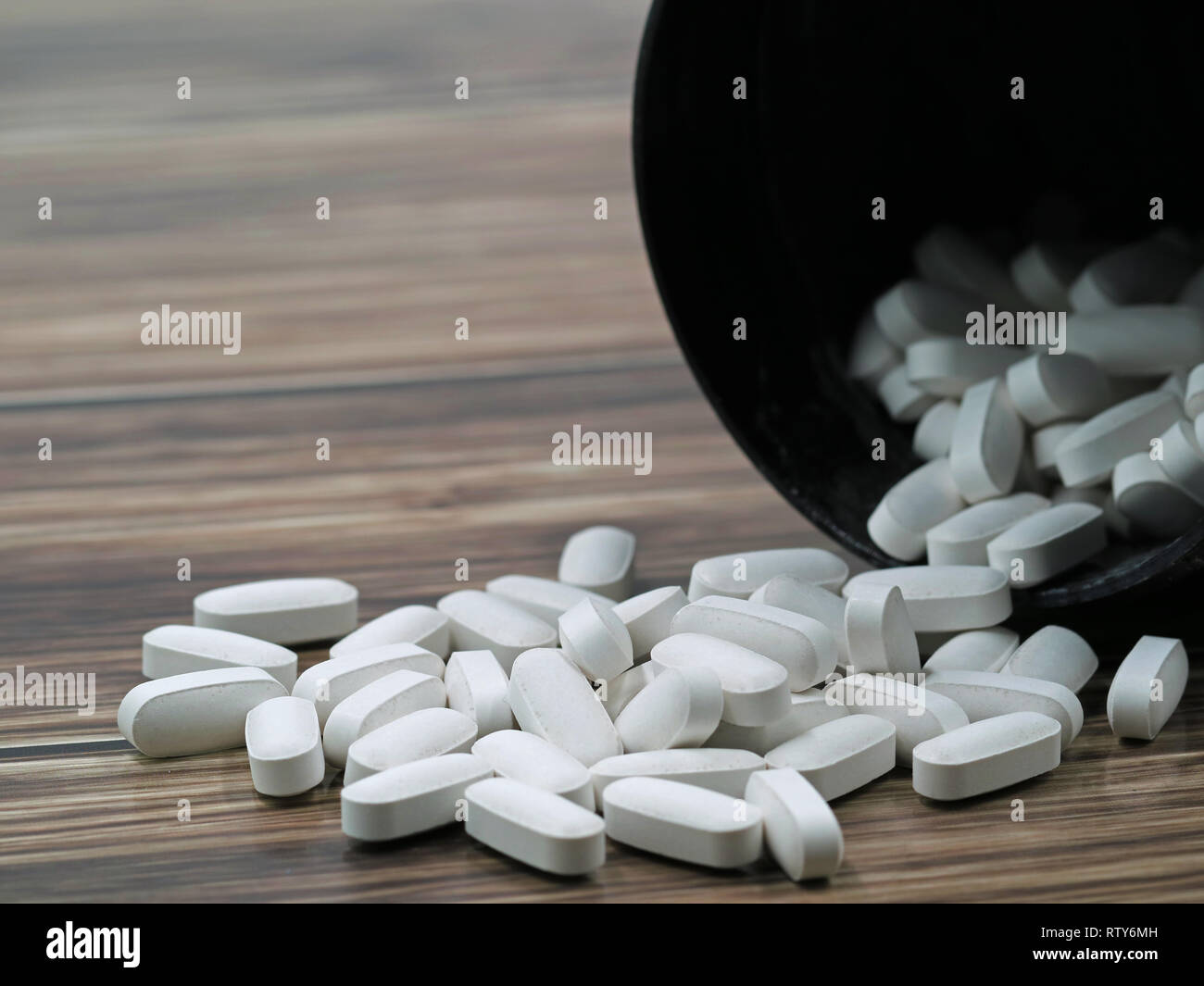 White pills spilling out of a toppled dark pill bottle on wooden ground, copy space Stock Photo