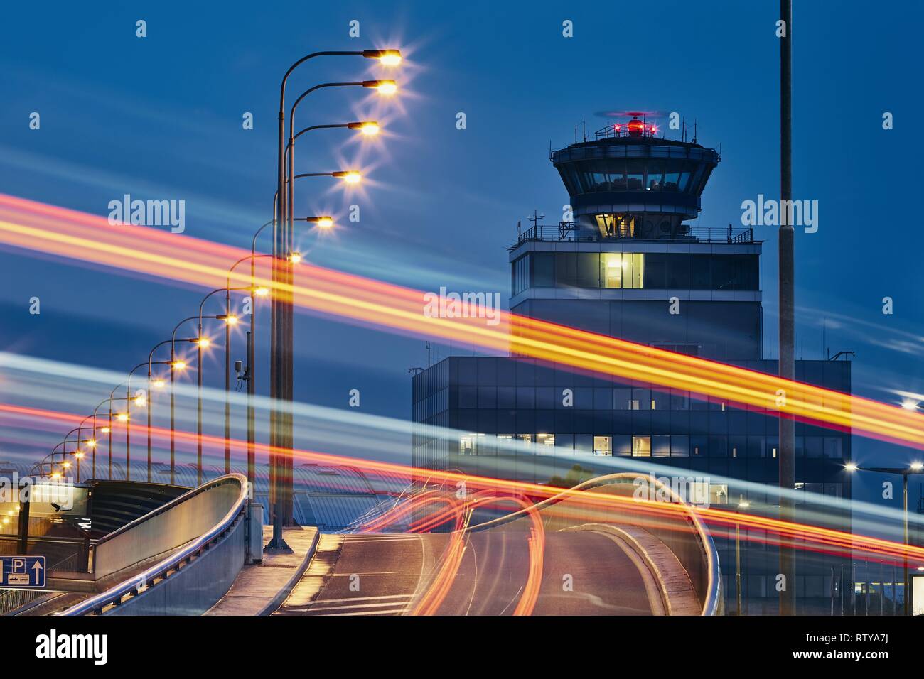 Light trails of the cars on the road to airport against air traffic control tower. Stock Photo