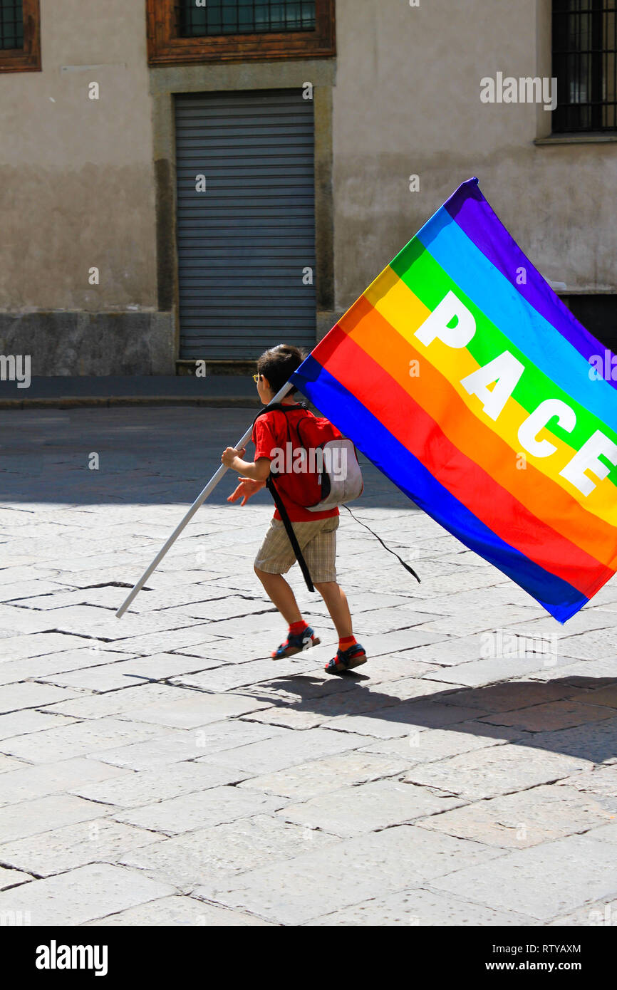 Unidentified child with rainbow flag with 'peace' (Latin and Italian: Pace) written on it, in a  bad abondoned neighbourhood. Concept of world peace a Stock Photo