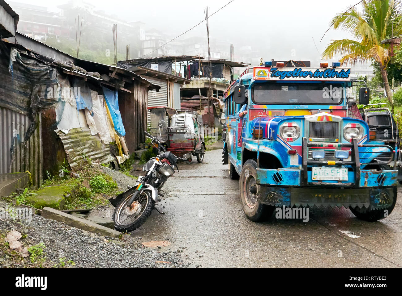 Banaue, Ifugao Province, Philippines - December 19, 2017: Scene of colorful jeepney riding on a road in Banaue, surrounded by typical poor shelters Stock Photo