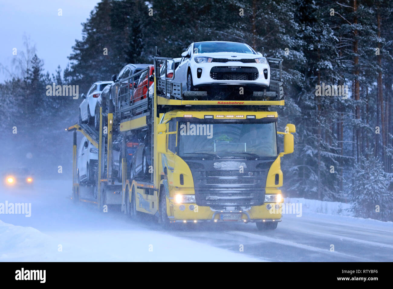 Salo, Finland - January 18, 2019: Yellow Scania car carrier truck travels in the snow trail of another vehicle on a day of winter snowfall in Finland. Stock Photo