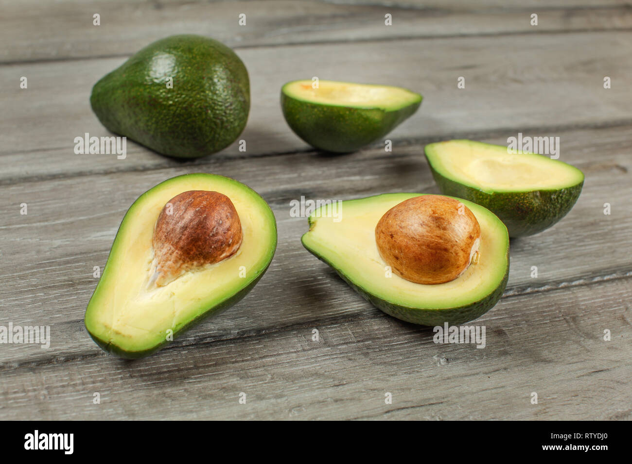 Avocados cut in half seed visible, one whole green pear in background, on  gray wood desk Stock Photo - Alamy