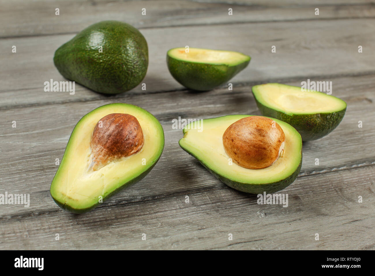 Avocados Cut In Half Seed Visible One Whole Green Pear In Background On Gray Wood Desk Stock Photo Alamy