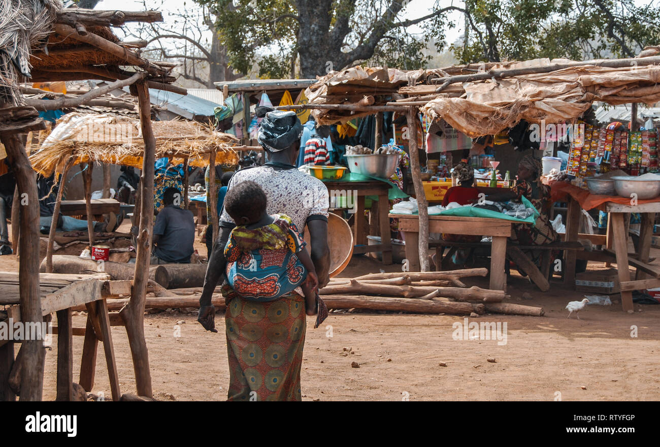 A photo of a mother carrying her child walking at the marketplace in Bolgatanga Stock Photo