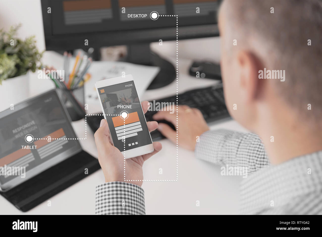 Web designer, programmer working with responsive web template. Multiple devices on desk. Stock Photo