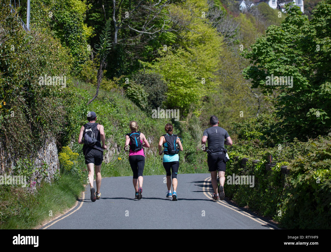 A shot of a group of joggers jogging along Cliff Road towards Salcombe during the summer. Stock Photo