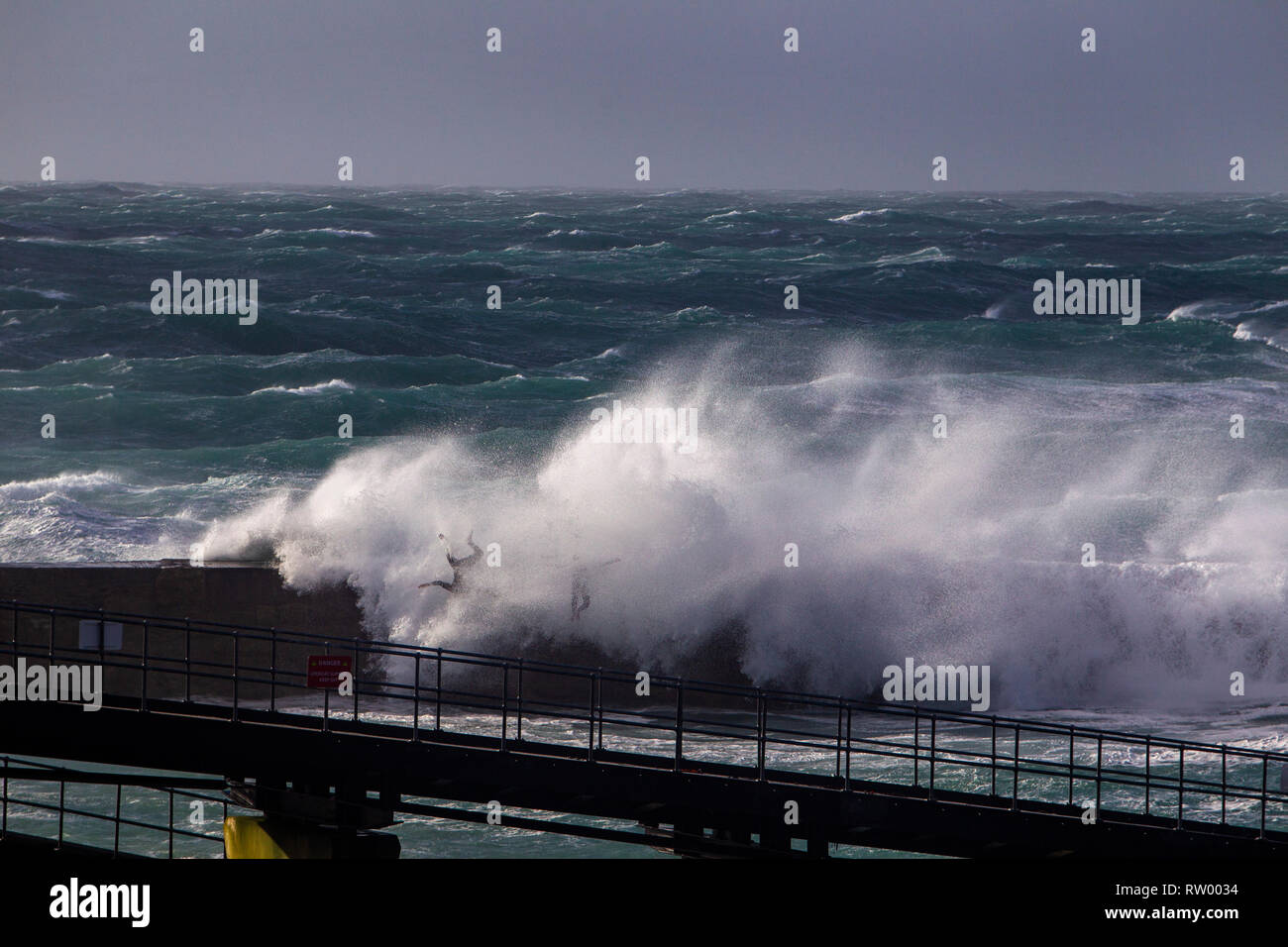 Sennen, Cornwall, UK. 3rd  March 2019. Gale force winds and 20ft high waves lash the granite cliffs of Cornwall. Daring jumpers get caught by some huge waves swamping the pier. Credit: Mike Newman/Alamy Live News. Stock Photo