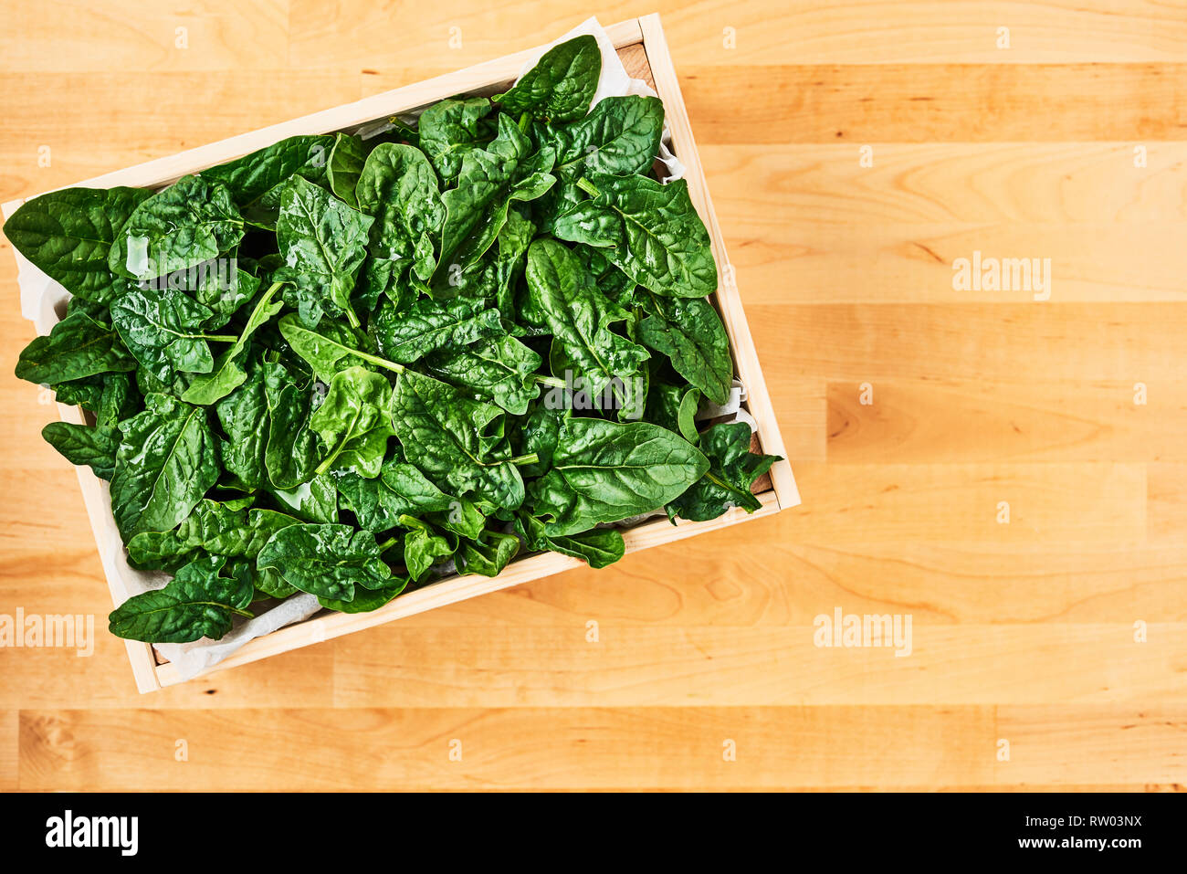 Fresh spinach leaves with water drops in wooden box on wooden table. Top view with copy space for text. Stock Photo