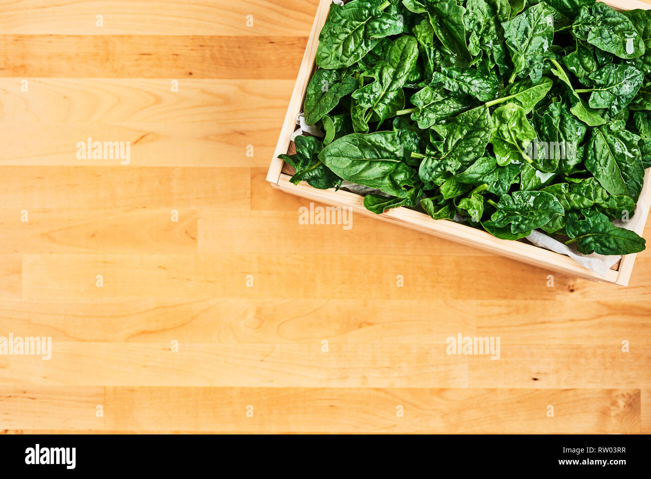 Fresh spinach leaves with water drops in wooden box on wooden table. Top view with copy space for text. Stock Photo