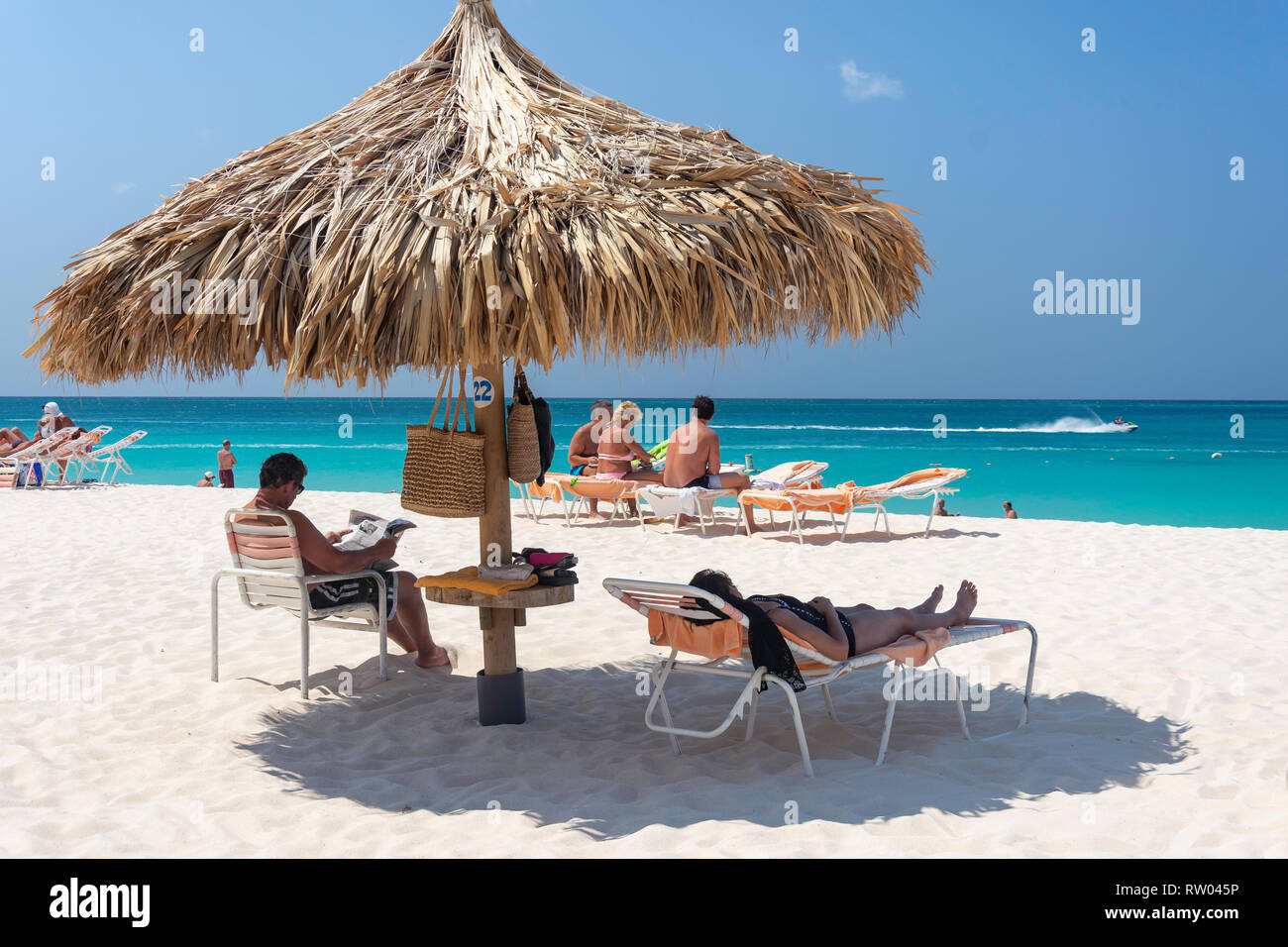 Couple relaxing under straw parasol,  Eagle Beach, Oranjestad District, Aruba, ABC Islands, Leeward Antilles, Caribbean Stock Photo