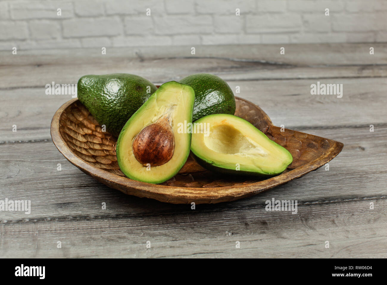 Avocado Cut In Half Seed And Pulp Visible Two More Whole Pears On Carved Wooden Bowl Stock Photo Alamy