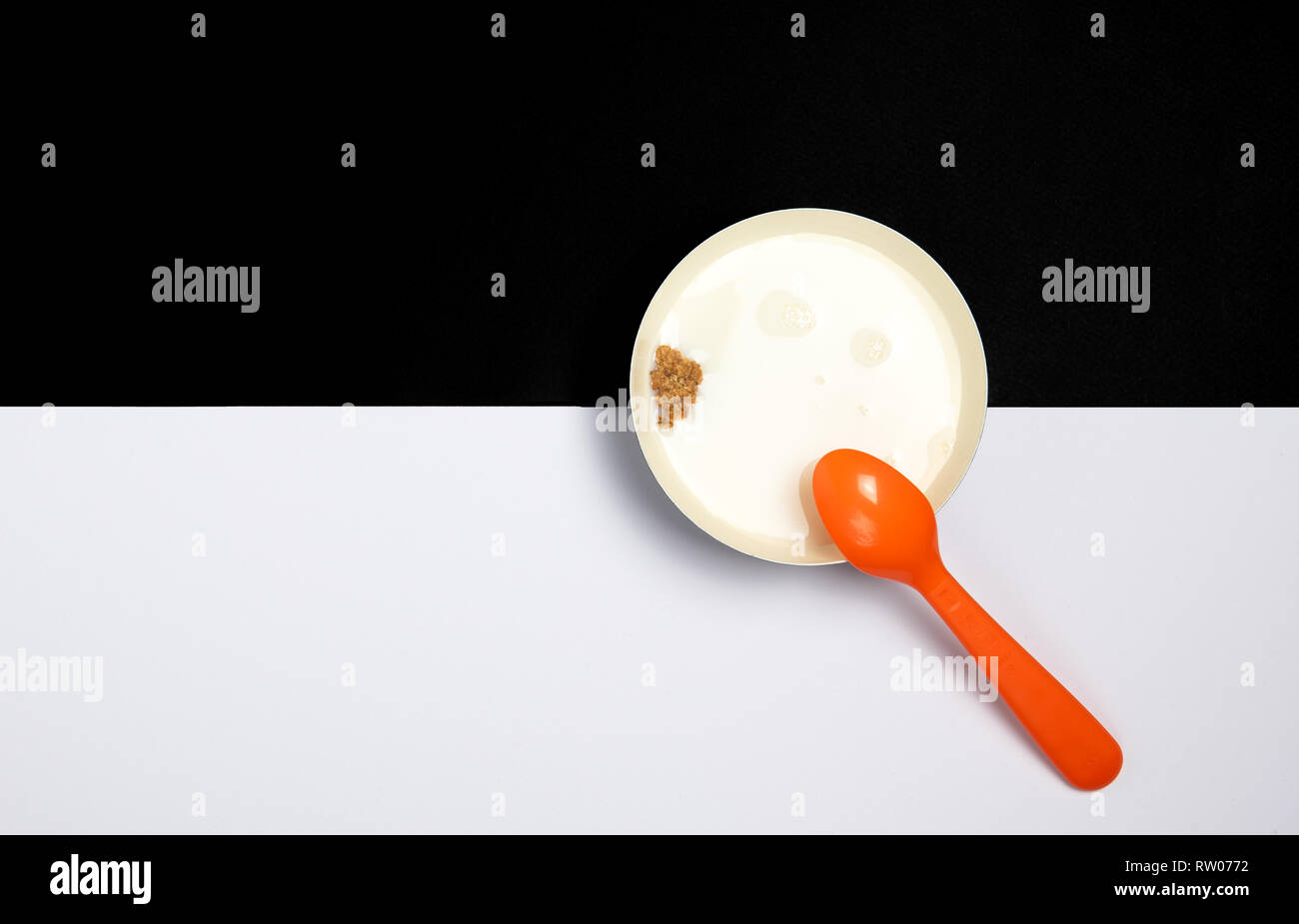 Ceramic bowl filled with milk and a piece of healthy cereal and an orange spoon on a black and white background. Concept of healthy breakfast Stock Photo