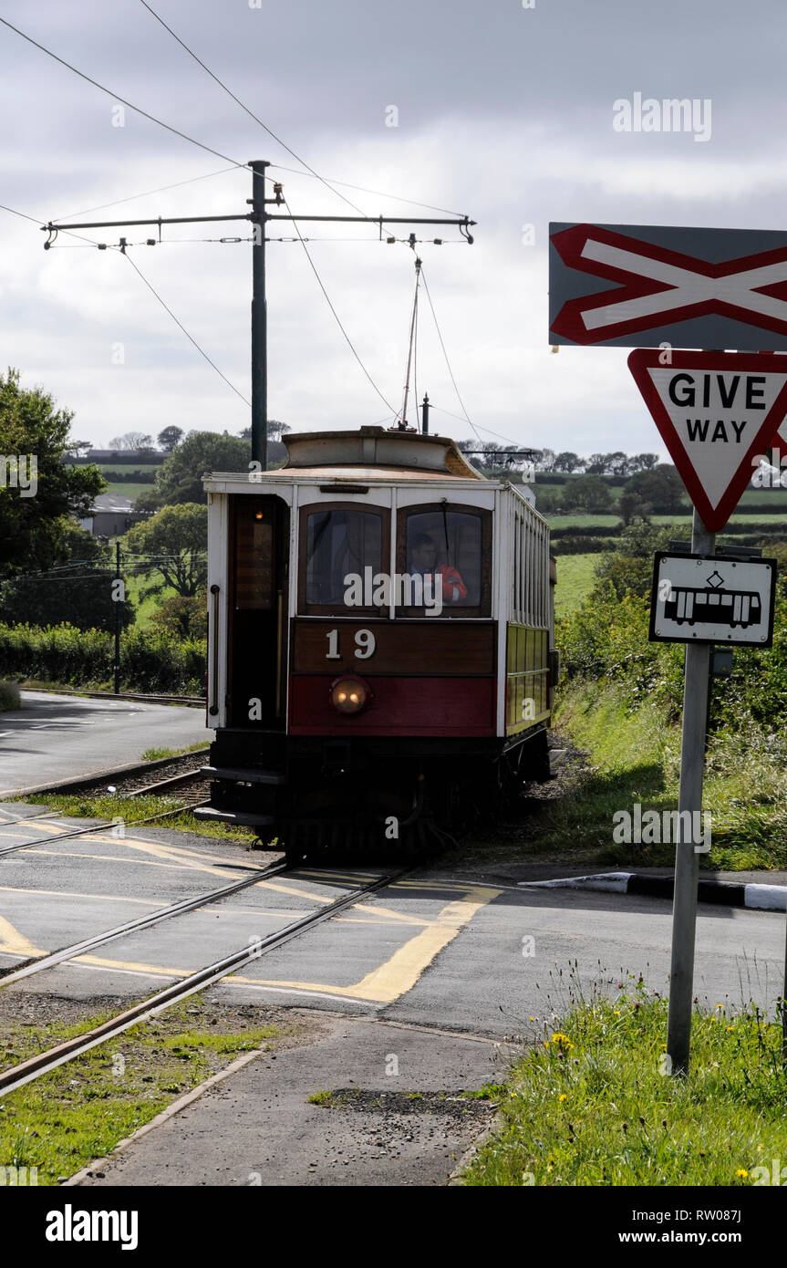 An electric tram trundles over a tram/ road crossing on the 17 miles long, rail track connecting Ramsey and Douglas on the Isle of Man, Britain.  A fl Stock Photo