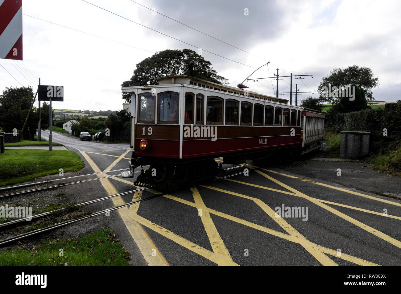 An electric tram trundles over a tram/ road crossing on the 17 miles long, rail track connecting Ramsey and Douglas on the Isle of Man, Britain.  A fl Stock Photo