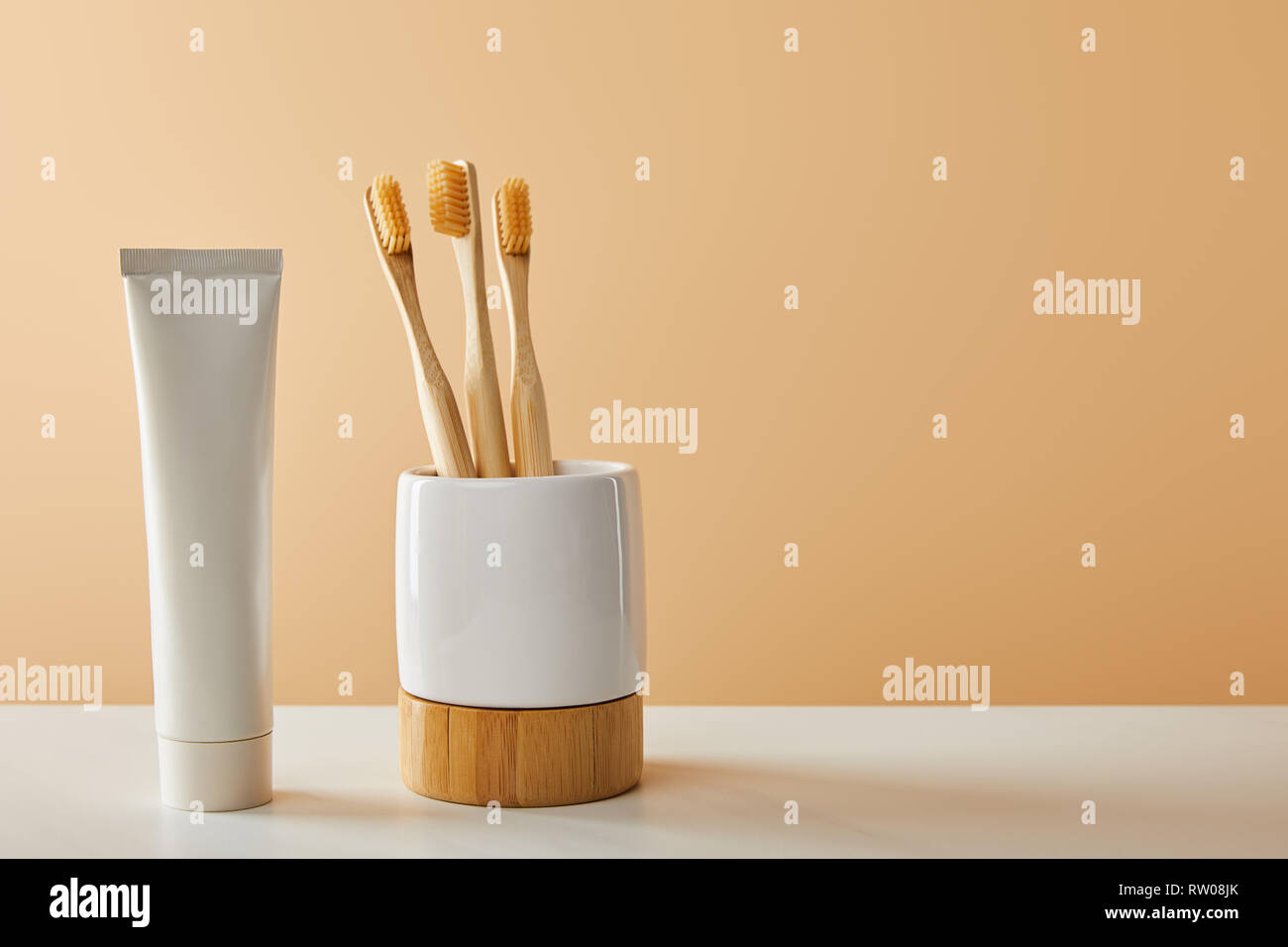 bamboo toothbrushes in holder and toothpaste in tube on white table and ...