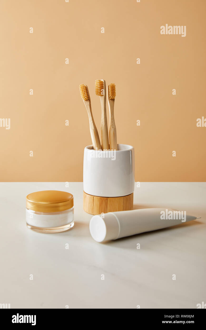bamboo toothbrushes in holder, toothpaste in tube and cosmetic cream on ...