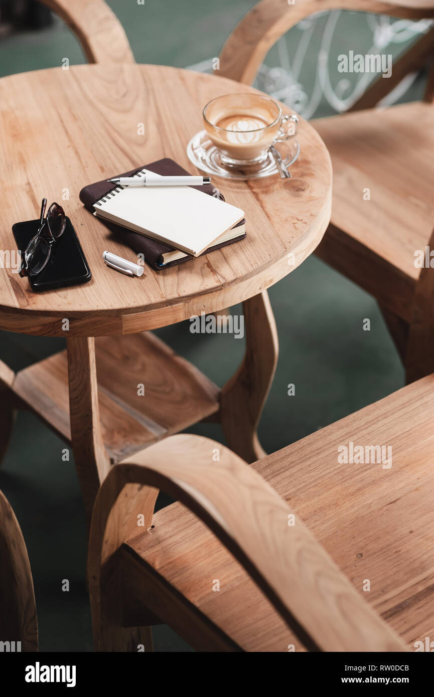 Abstract scene of opened small notebook, pen, glasses, mobile phone, and coffee cup on wood counter. Coffee break and relax time. Working from anywher Stock Photo