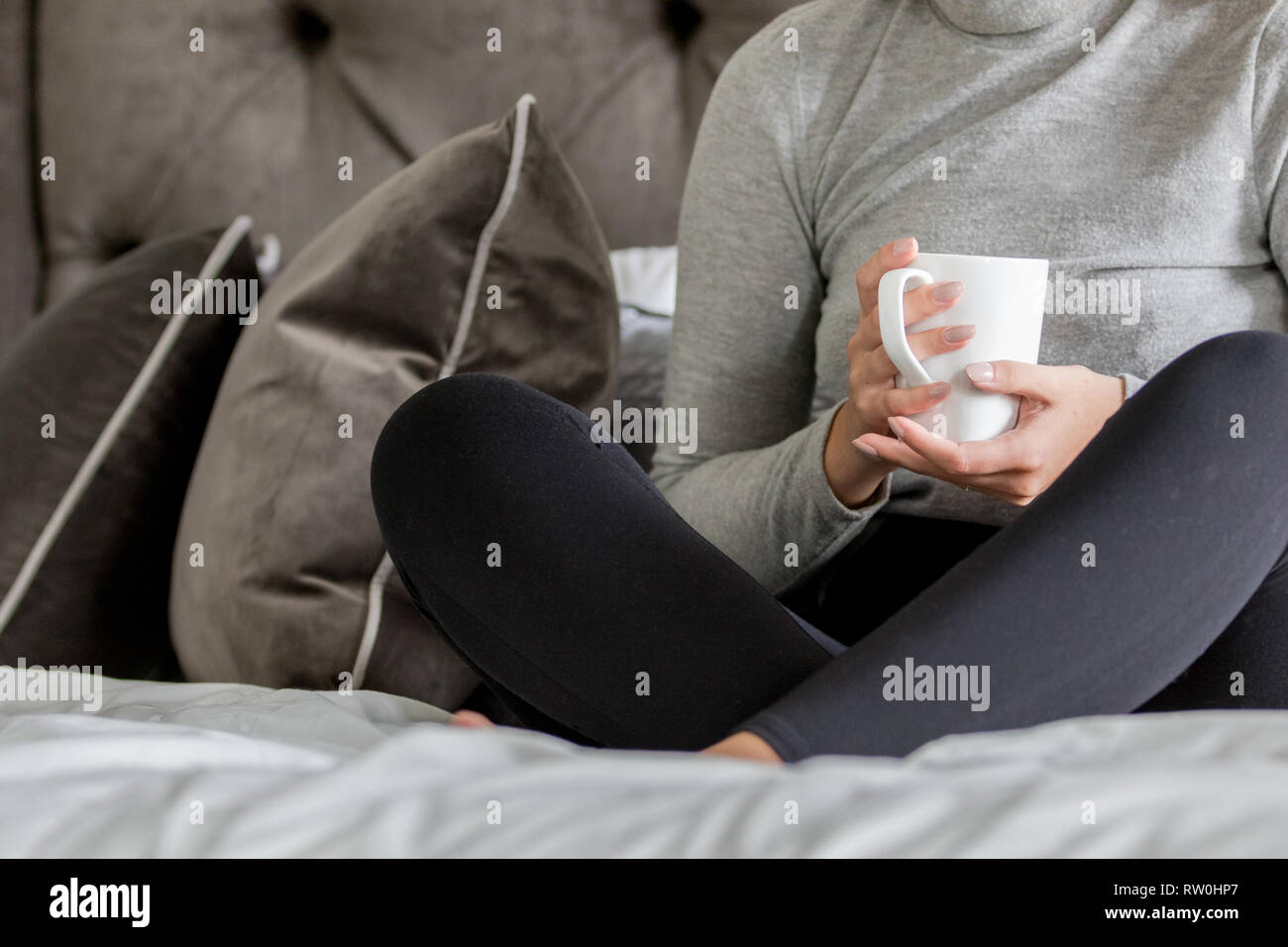 A young woman sitting on a bed with a white coffee mug Stock Photo