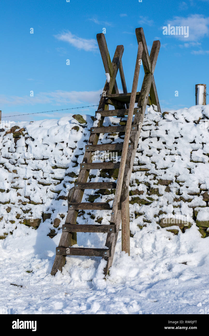 Snow covered dry stone wall in the Derbyshire Peak District,  Ladder style against a cold blue sky. Stock Photo