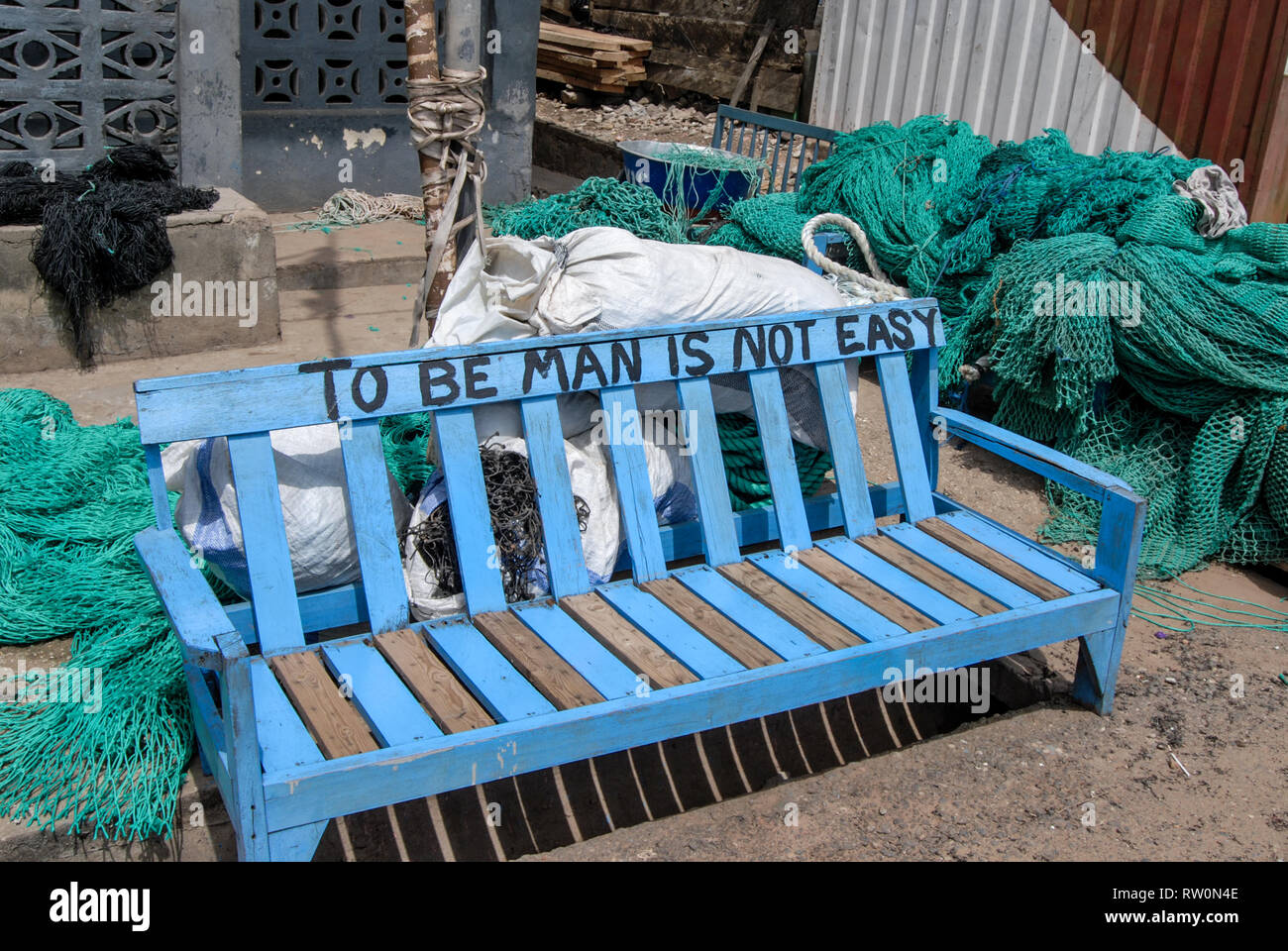 To be man is not easy - an interesting message on a blue street bench at the harbour of Elmina, Ghana, West Africa Stock Photo