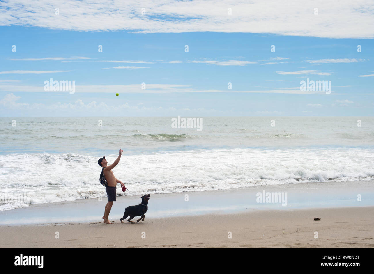 BALI, INDONESIA - JANUARY 16, 2017: Man playing ball with pet dog at the beach, cloudy wetaher Stock Photo