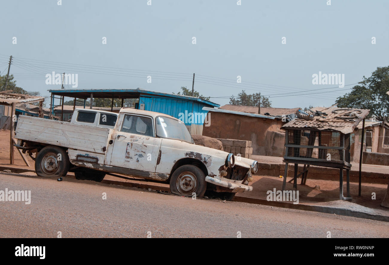 A old white car with flat tires parked at a road in Ghanaian town Bolgatanga, Ghana, West Africa Stock Photo