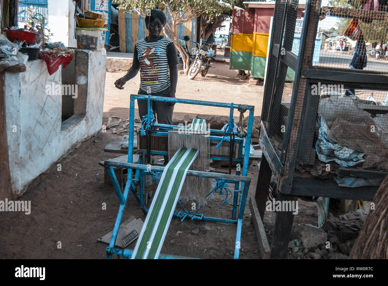 A photo of a local Ghanaian business woman operating a blue weaving machine on a street of Bolgatanga. Stock Photo