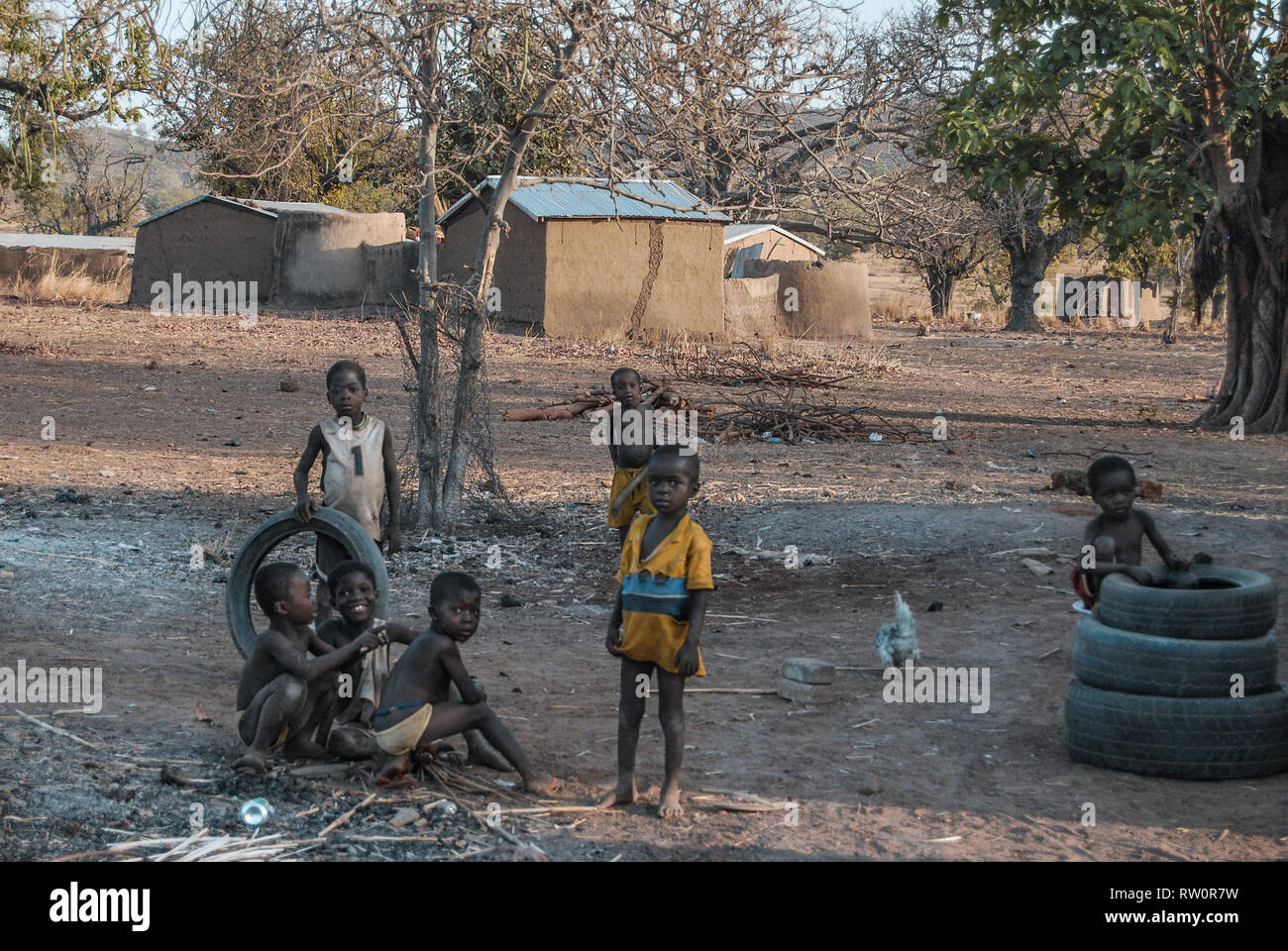A photo of Ghanaian children posing for the camera as they are playing with old car tyres in the yard. Taken in a savanna of Ghana. Stock Photo