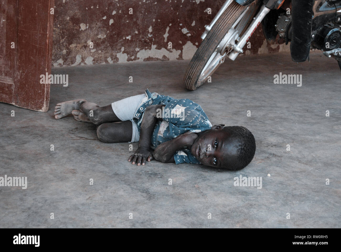 A dramatic and sad photo of a sick crying boy laying on a dirty floor begging for help. Child had strong pain in the stomach and noone could help him. Stock Photo