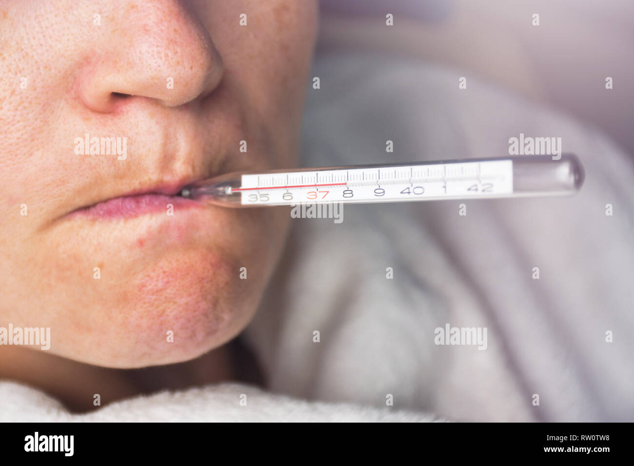 Sick woman with seasonal flu measuring body temperature with thermometer in her mouth reaching 38 degrees celsius Stock Photo