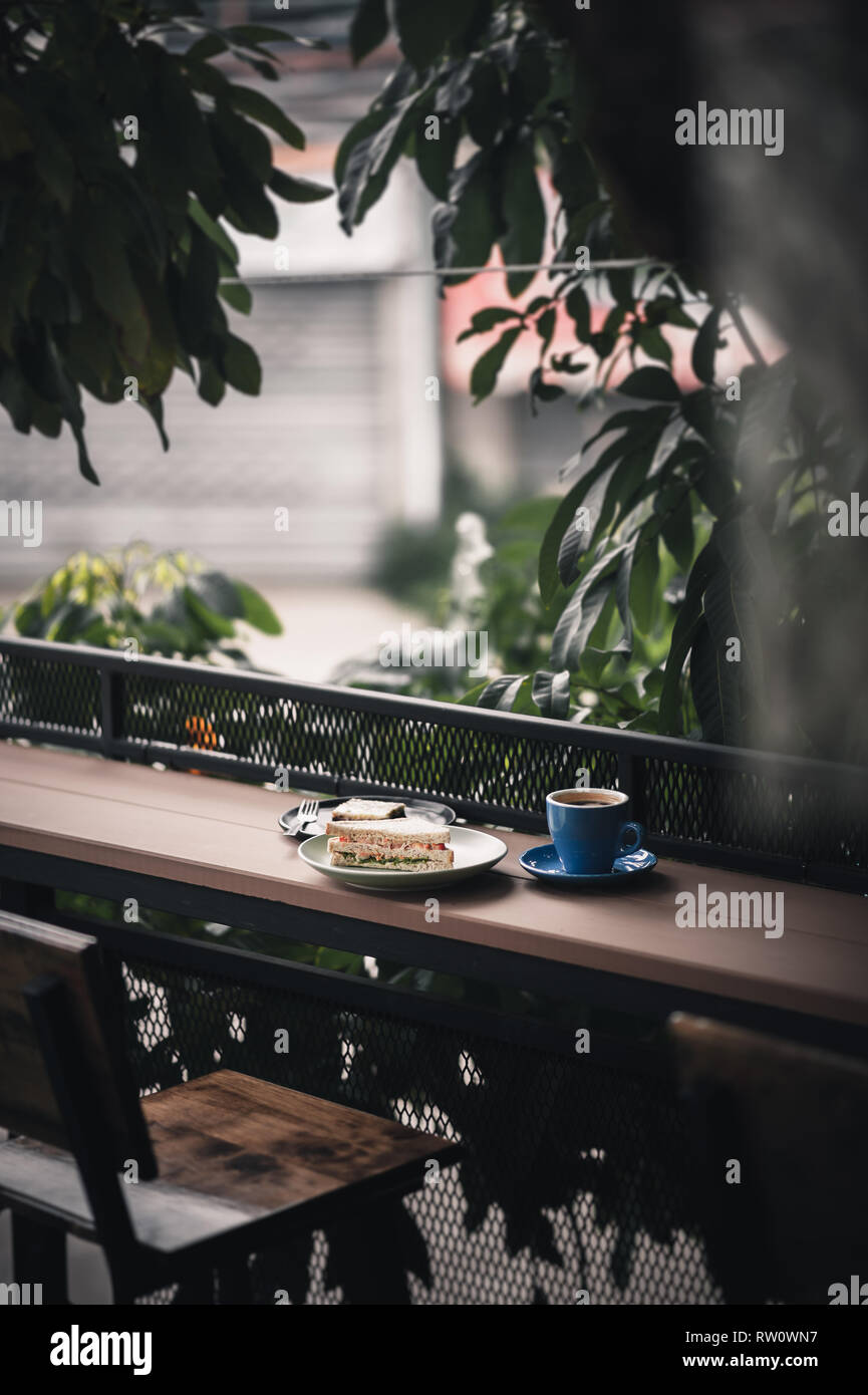 Abstract scene of breakfast meal set including tuna sandwich, hot long black coffee, and brownie cheese cake on outdoor wood bar. Weekend morning acti Stock Photo