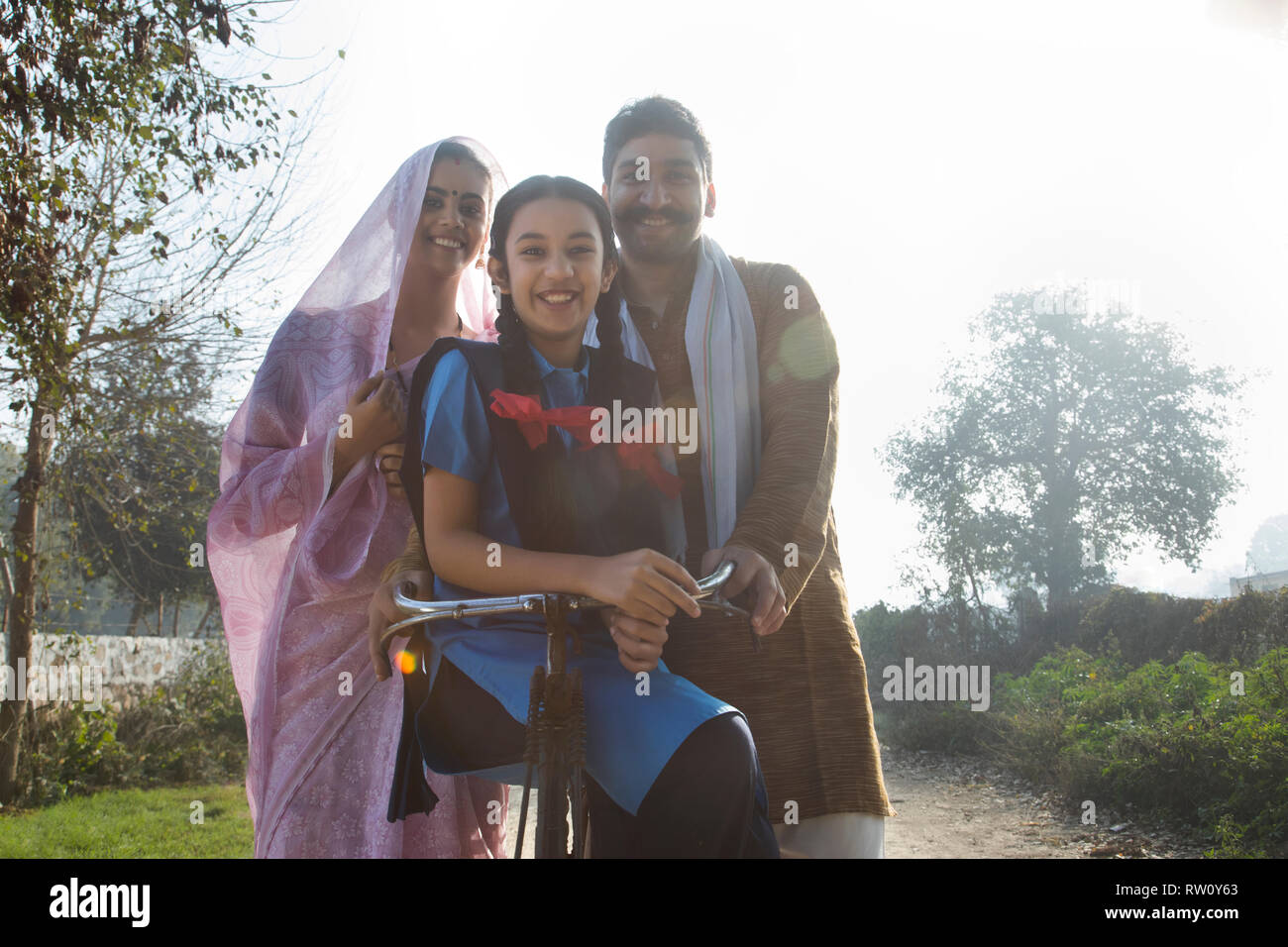 Low angle view of a happy rural family consisting of man, woman and a school going girl standing on pathway in a village. Stock Photo