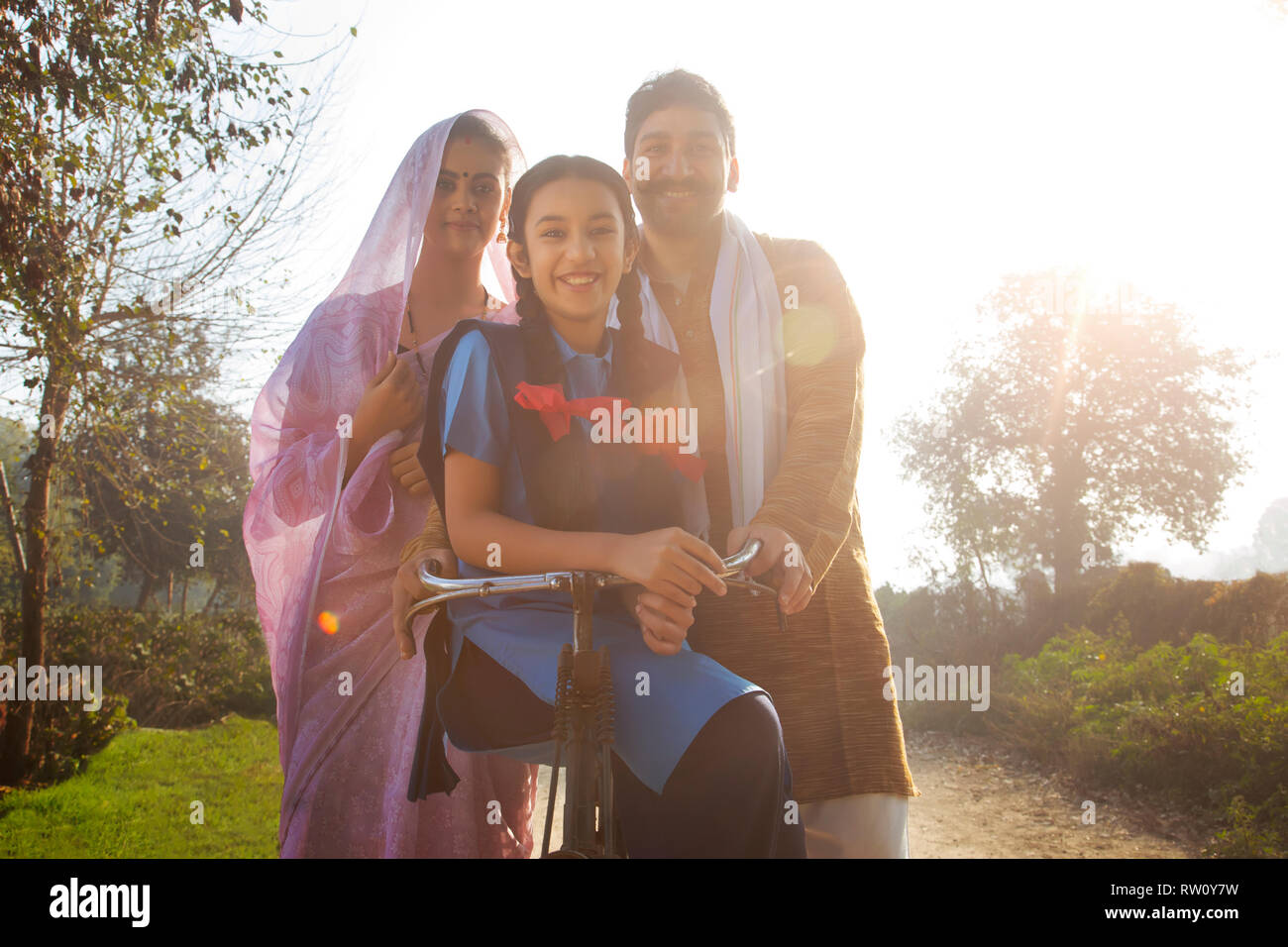 Low angle view of a happy rural family consisting of man, woman and a school going girl standing on pathway in a village. Stock Photo
