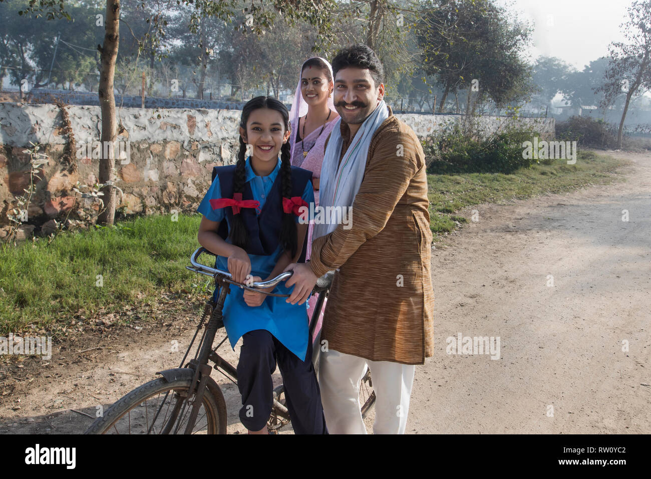 Happy rural family consisting of man, woman and a school going girl walking on street in a village. Stock Photo