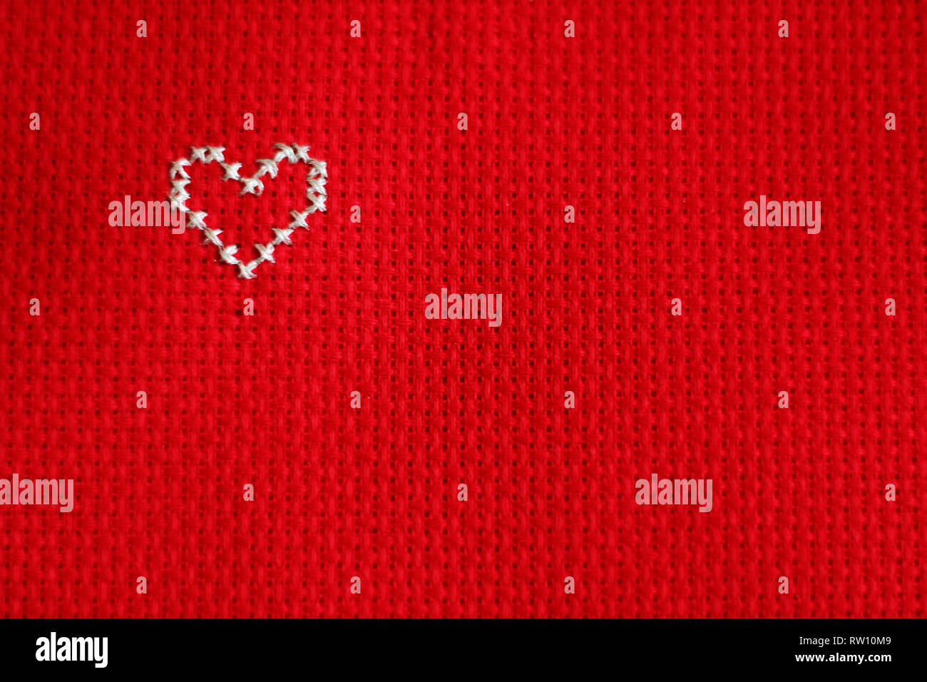 Cross stitched silver heart, left up side, red background. Free copy space Stock Photo