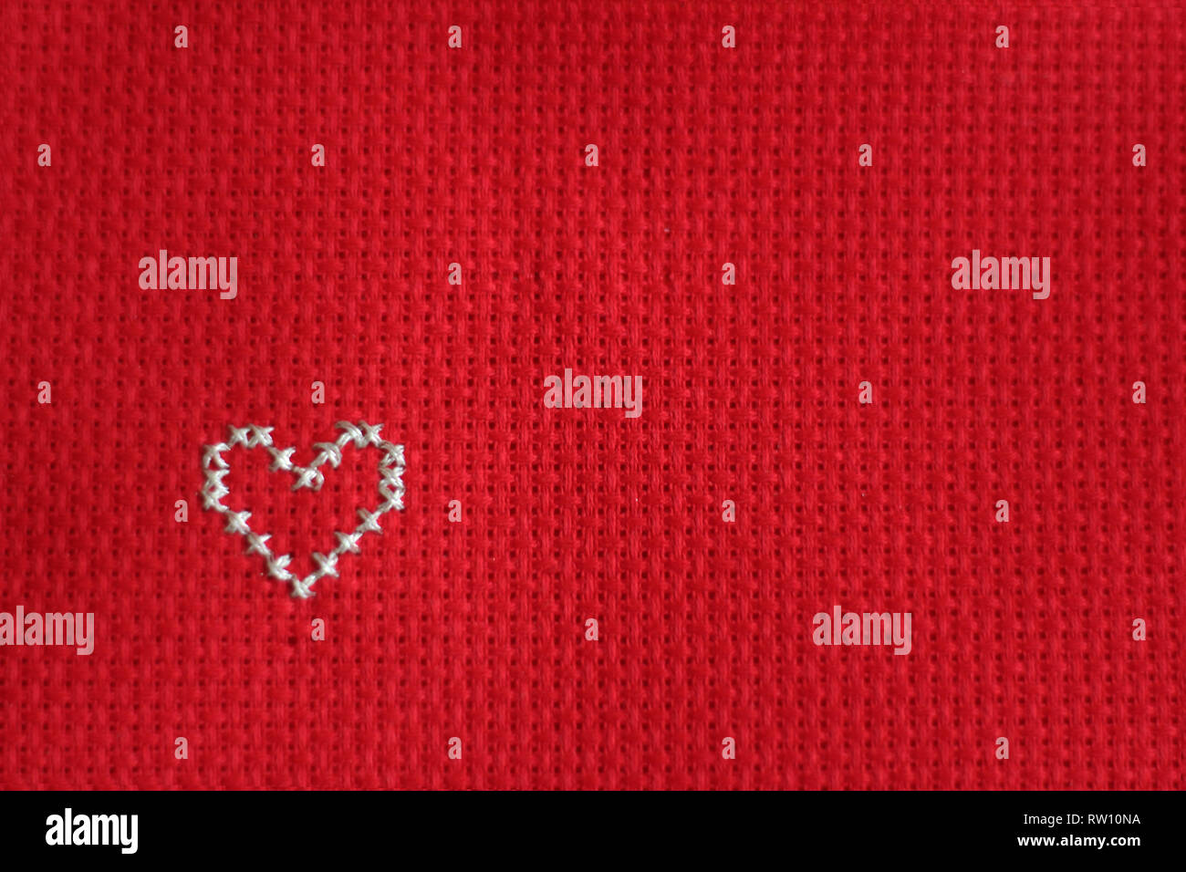 Cross stitched silver heart, red background. free copy space Stock Photo