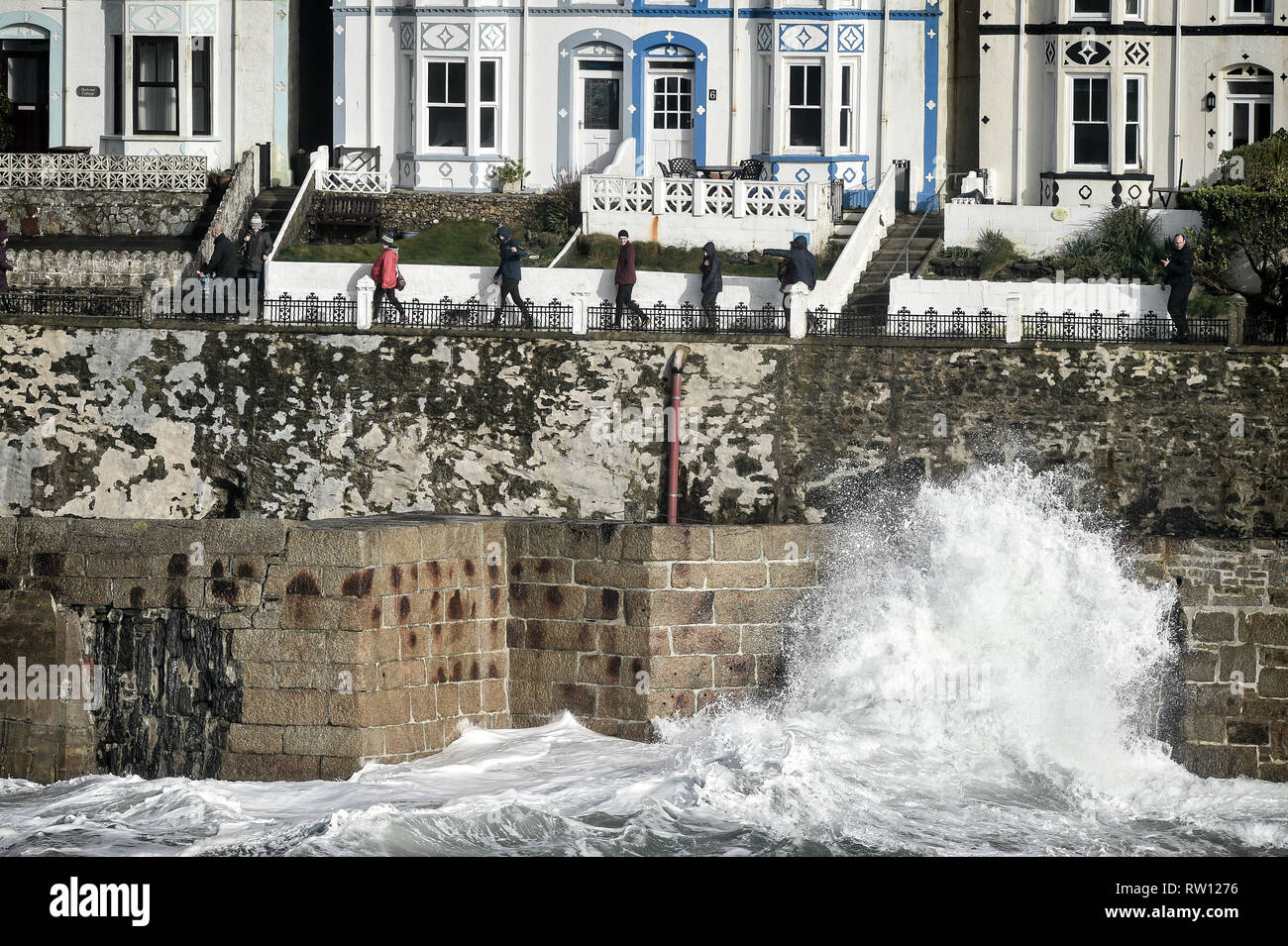 People walk along the top path instead of the road by the harbour to avoid waves at Porthleven, Cornwall. Storm Freya is set to bring strong winds of up to 80mph, dangerous conditions and travel disruption to England and Wales on Sunday. Stock Photo