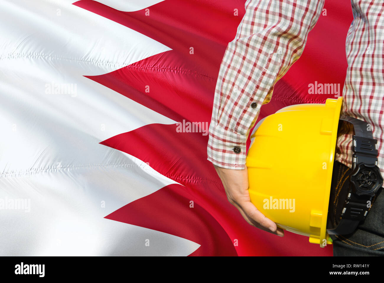 Bahraini Engineer is holding yellow safety helmet with waving Bahrain