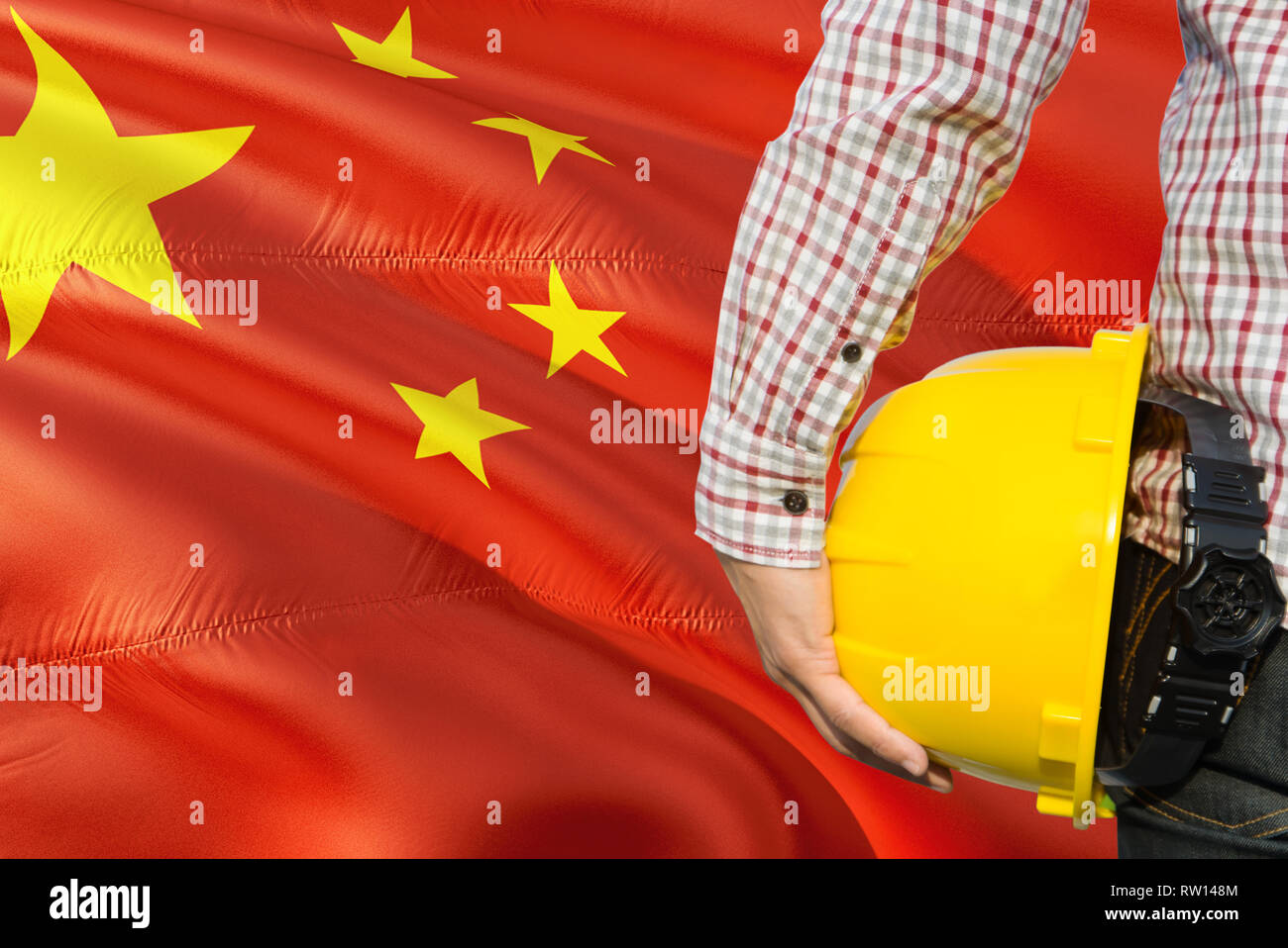 Chinese Engineer is holding yellow safety helmet with waving China flag